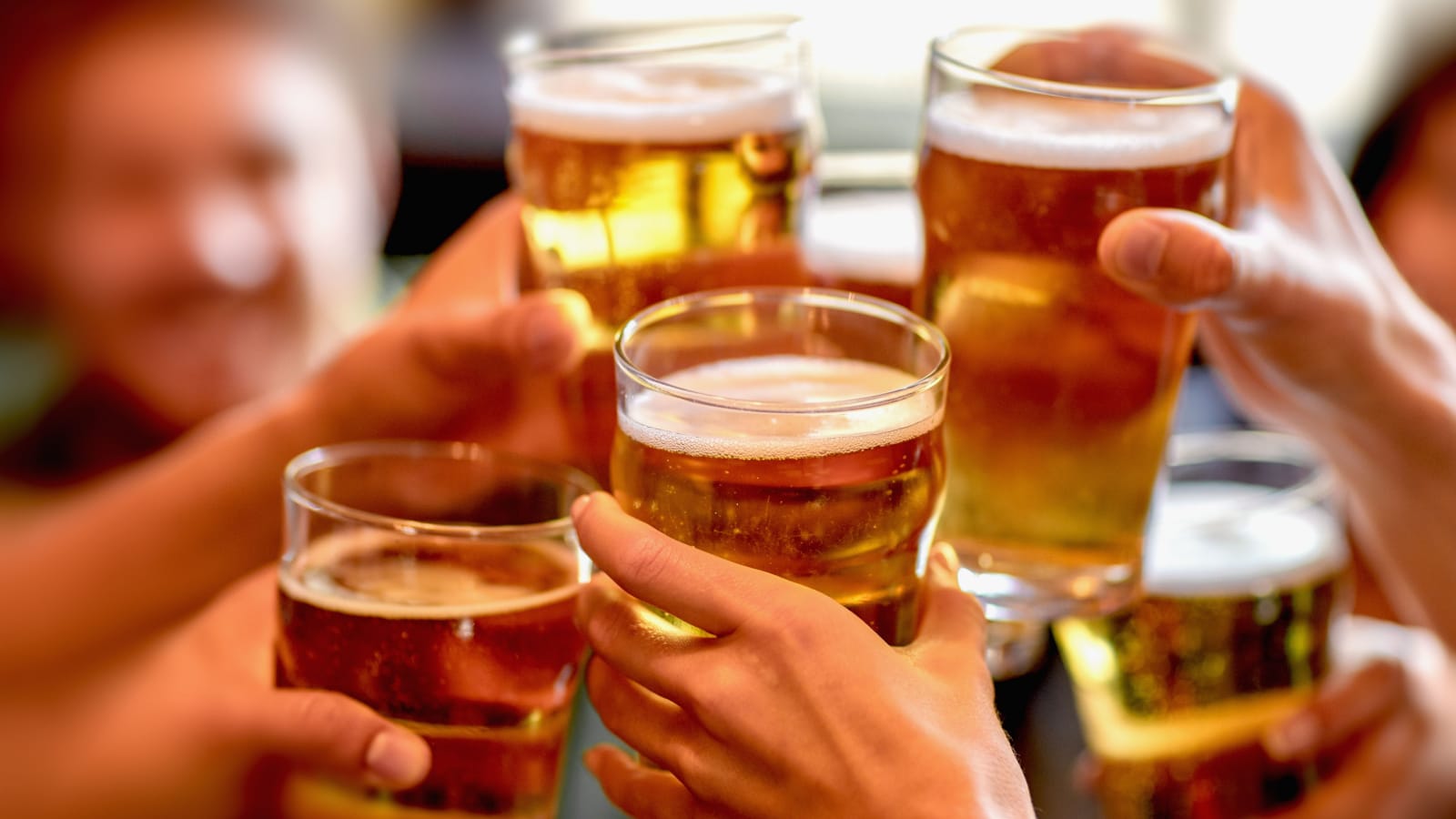 leisure, drinks, celebration, people and holidays concept - smiling friends drinking beer and stitching glasses in a restaurant or pub