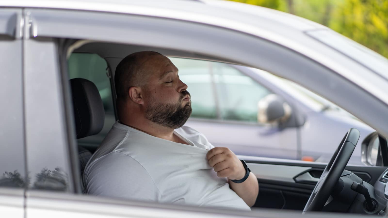 Exhausted man driver feeling blood pressure sitting inside car hot weather. Unwell overweight male stop after driving car in traffic jam suffering from overheat trying to cool down with windows open