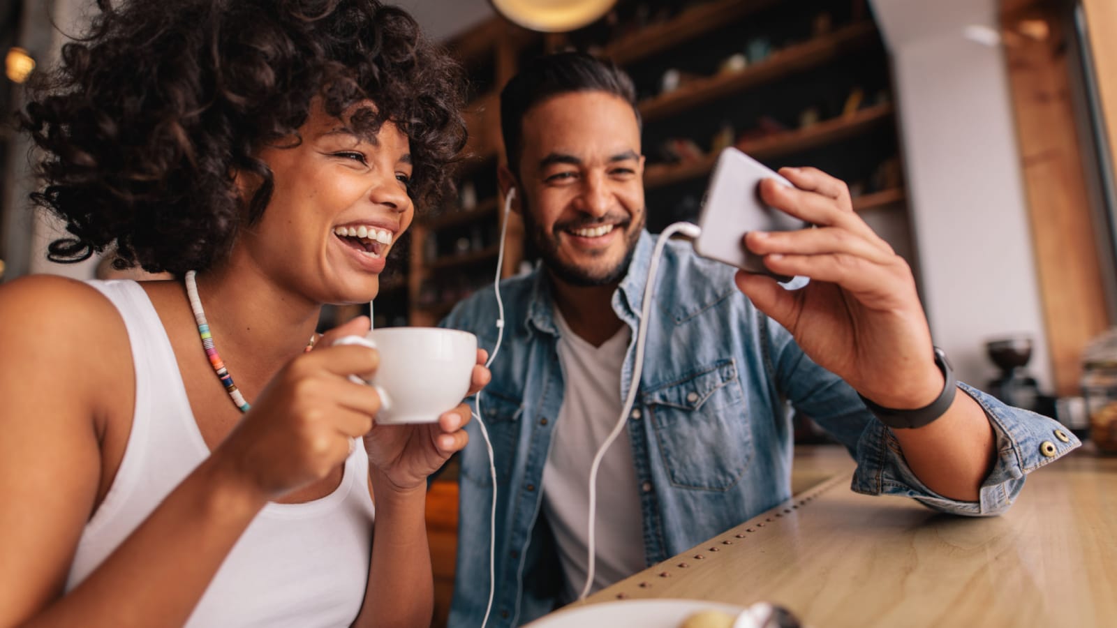 Young man showing something on cellphone to his girlfriend at cafe. Happy young couple sitting at coffee shop having video chat on mobile phone.