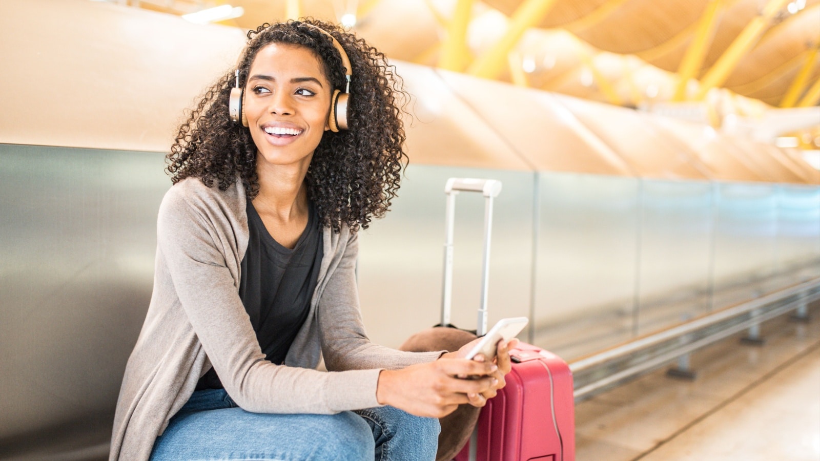 happy young woman listening music with headphones and mobile phone at the airport