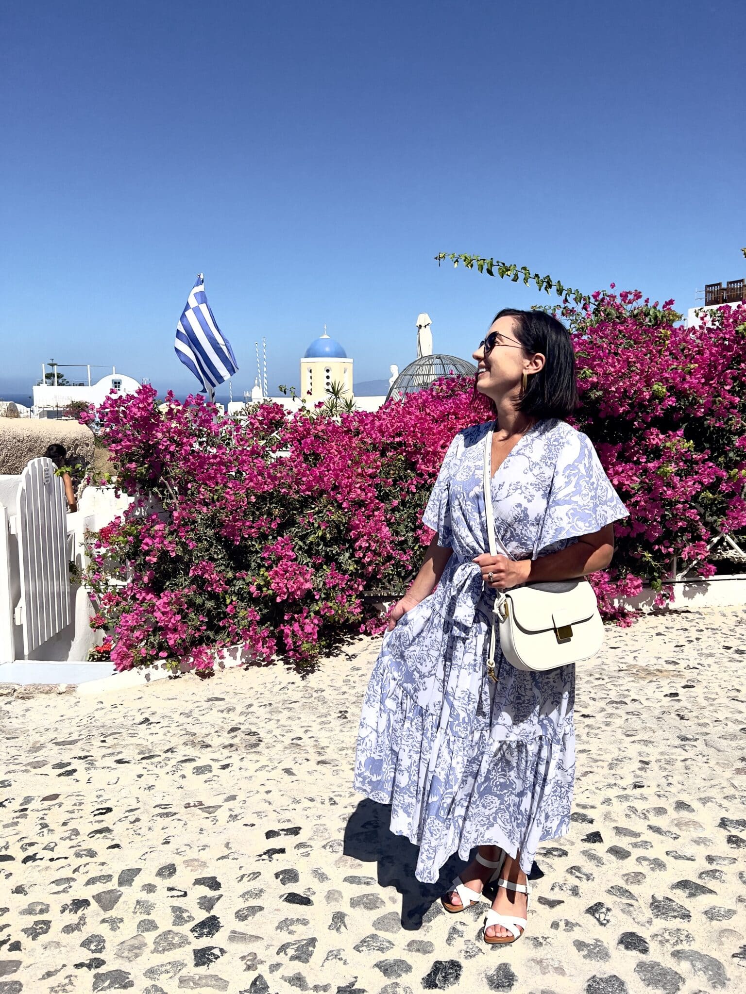 Lindsey of Have Clothes, Will Travel wearing a blue and white Chicwish maxi dress in Greece with pink flowers in the background