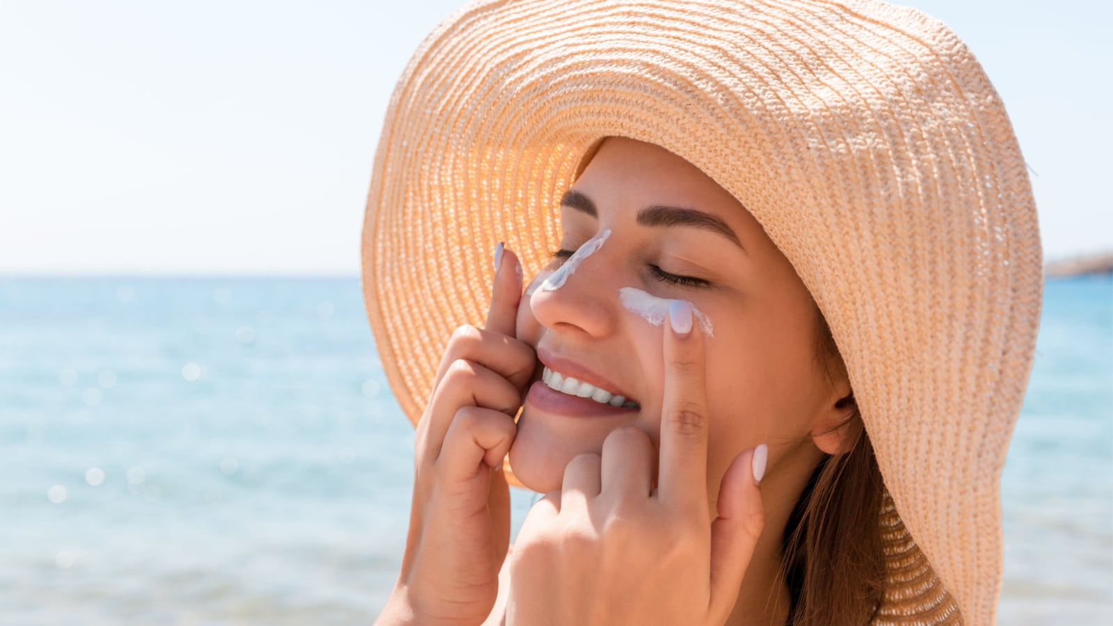 Smiling woman in hat is applying sunscreen on her face. Indian style.