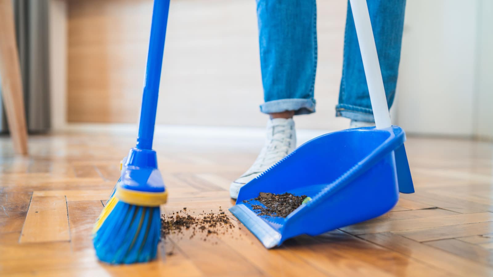 Portrait of young latin man sweeping wooden floor with broom at home. Cleaning, housework and housekeeping concept.