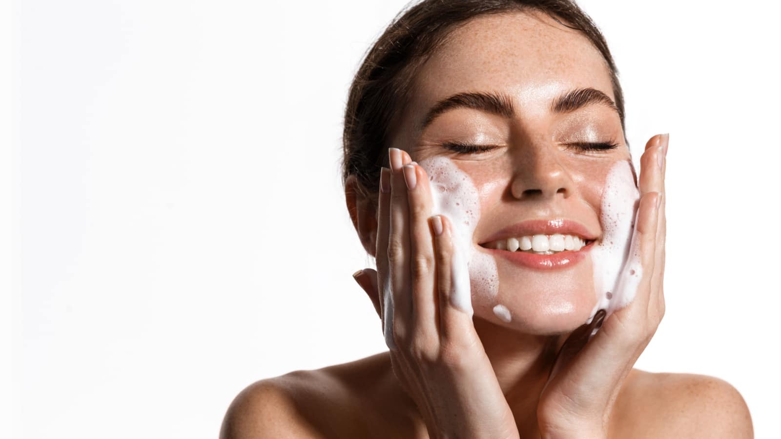 Portrait of cheerful laughing woman applying cleansing foam for washing face. Lovely brunette with attractive appearance. Skincare spa relax concept. Isolated on white background