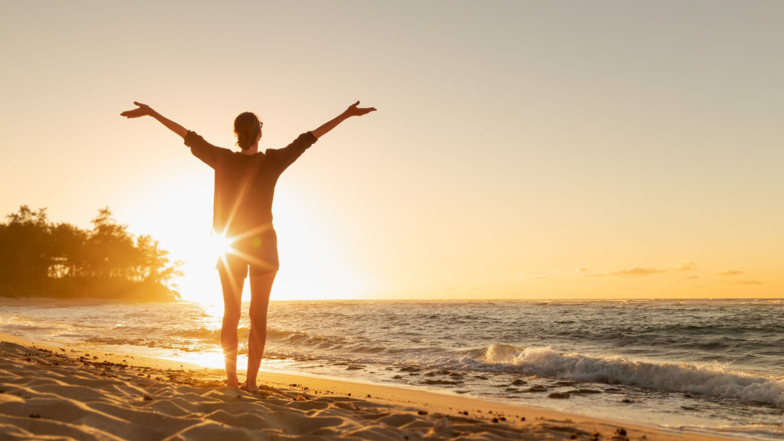 Female with arms up feeling the the energy and warmth of the sun on the beach at sunset