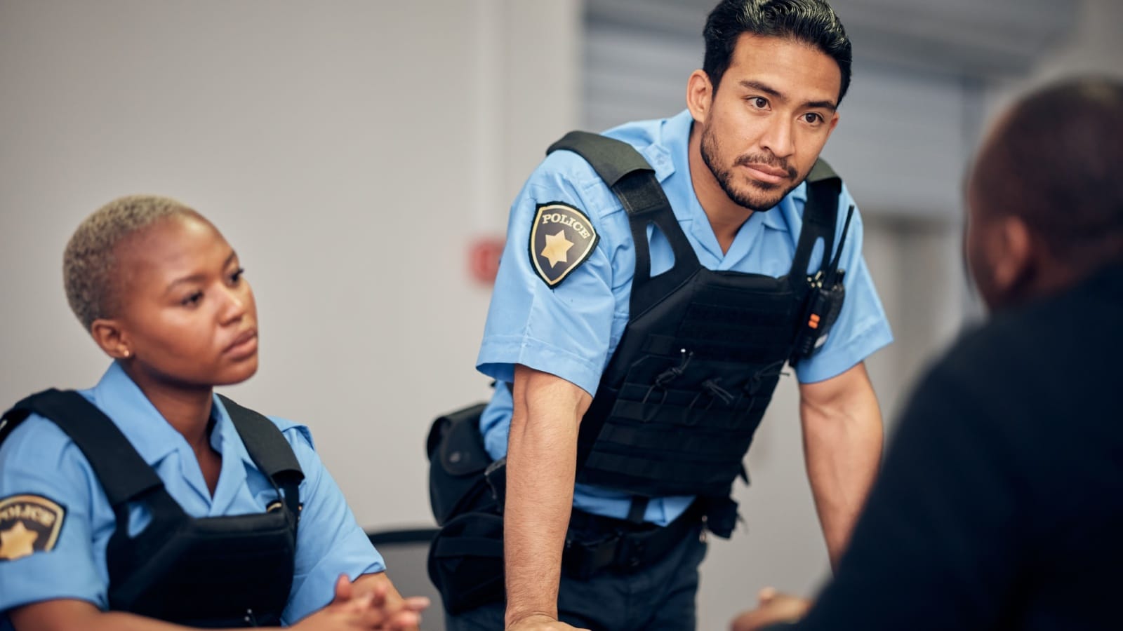 Interrogation, arrest and police team with a suspect for questions as law enforcement officers. Security, crime or investigation with a serious man and woman cop talking to a witness for information