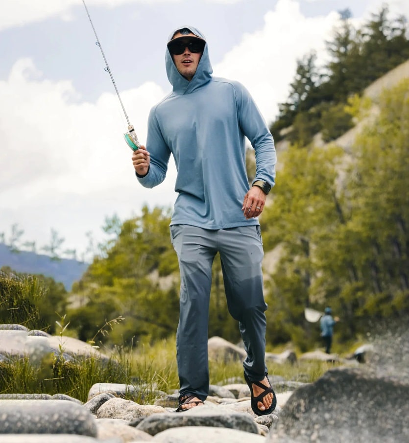 A man going fishing holding a rod and wearing a blue shirt and Men's Breeze Pant by Free Fly