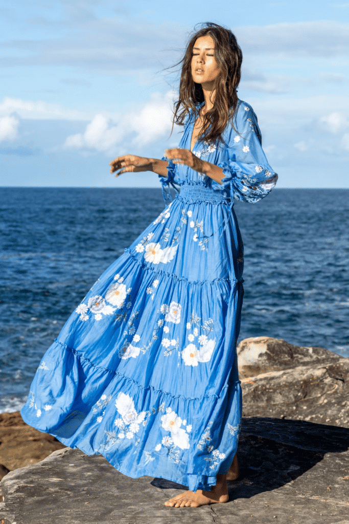 Woman wearing a flowy blue maxi dress by the ocean