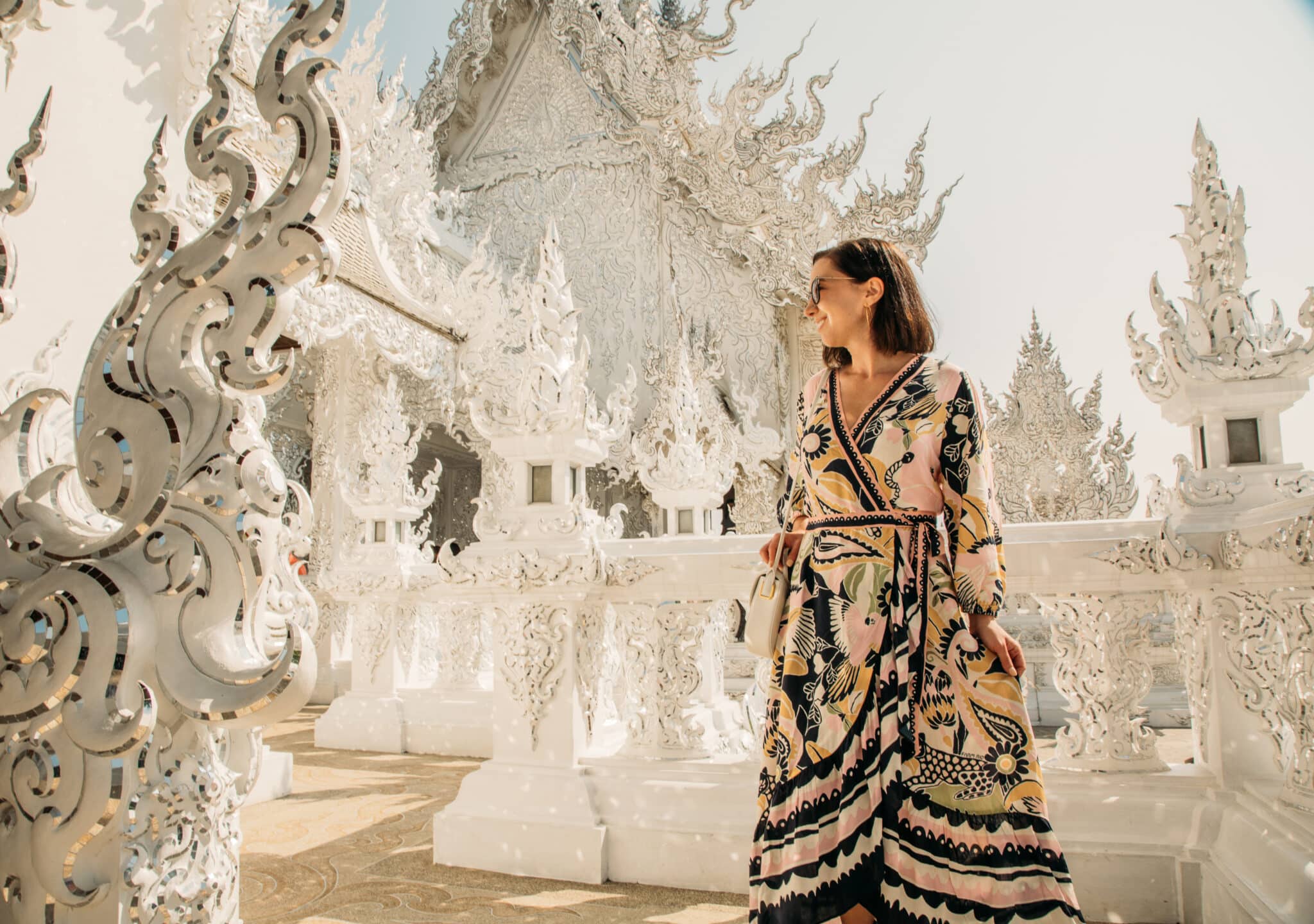 Lindsey wears a colorful Farm Rio wrap dress against a bright white temple in Thailand