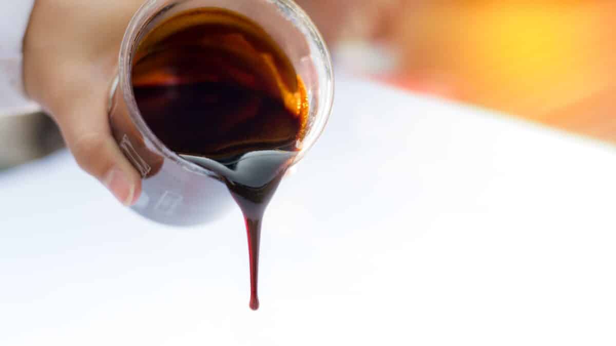 Droping molasses on beaker with hands in lab. Molasses is the final product from the sugarcane extraction process of sugar factory industrial. Background with copy and text space. - Selective focus.