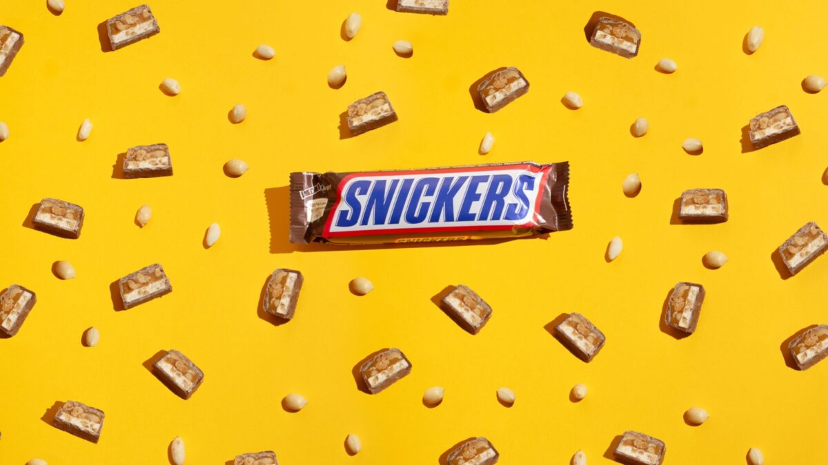 Kiev, Ukraine - March 6, 2021: Pieces of Snickers chocolate bar on a background of peanuts. Modern composition on yellow background