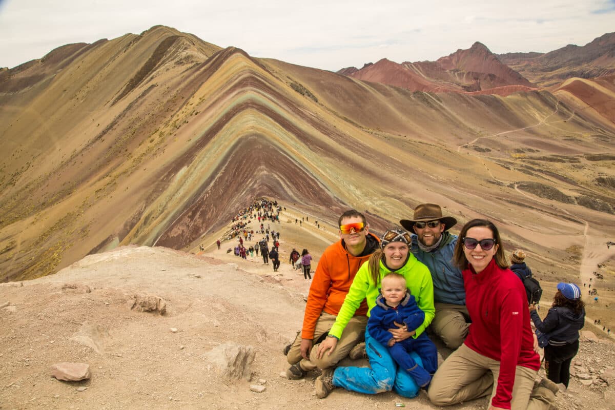 A group of adults and baby posing for a photo with Rainbow Mountain Peru in the background