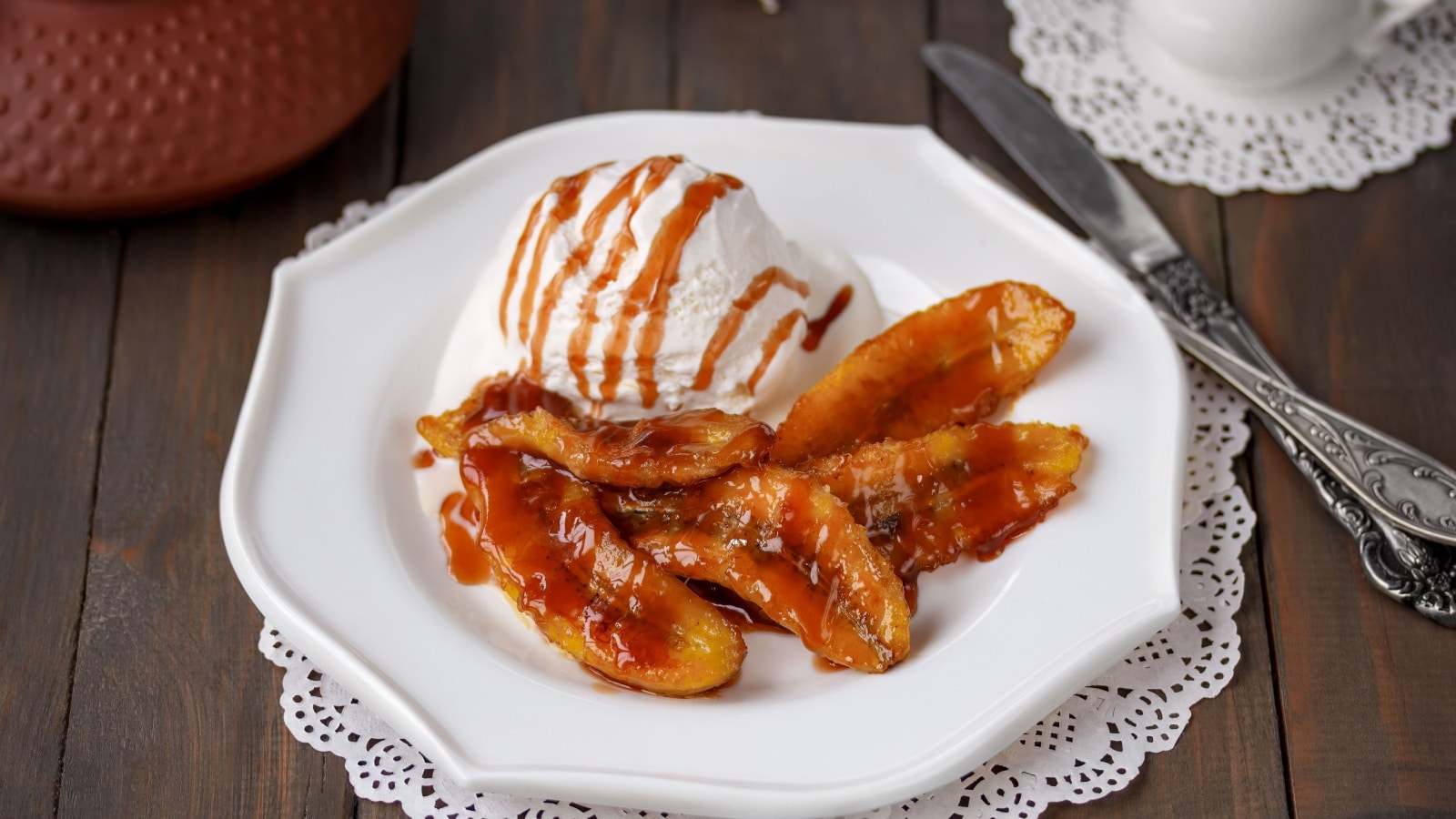 Bananas Flambe or Bananas Foster. A portion of sweet caramelized sliced bananas and a flambéed rum sauce served with scoop of vanilla ice cream on white plate. Selective focus, horizontal