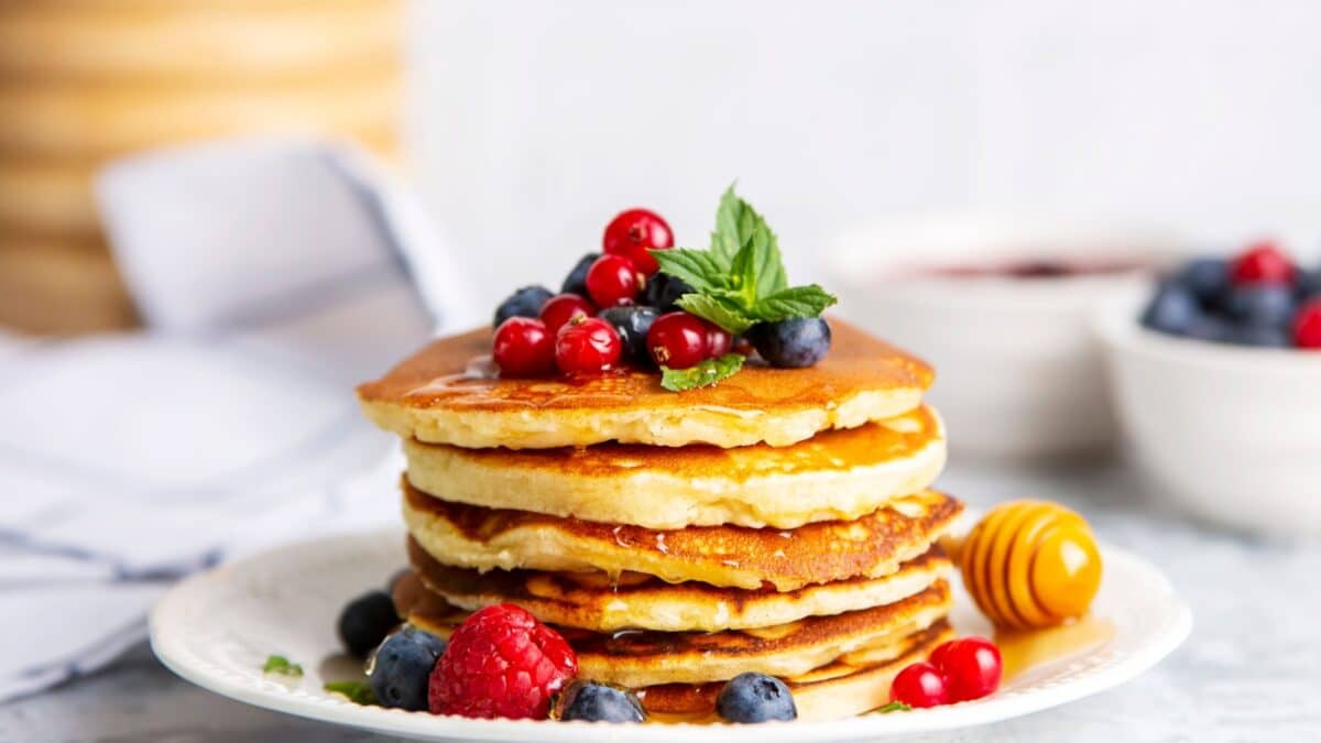 Healthy summer breakfast, homemade classic american pancakes with fresh fruit and honey, morning light gray stone background copy space top view