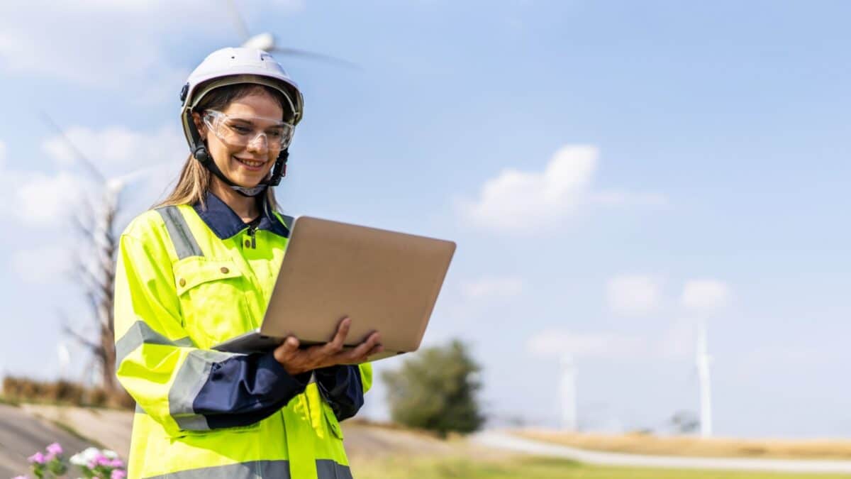 Caucasian woman engineer in uniform using laptop working stand near wind turbines farm, ecological energy industry, Environmental friendly for the future