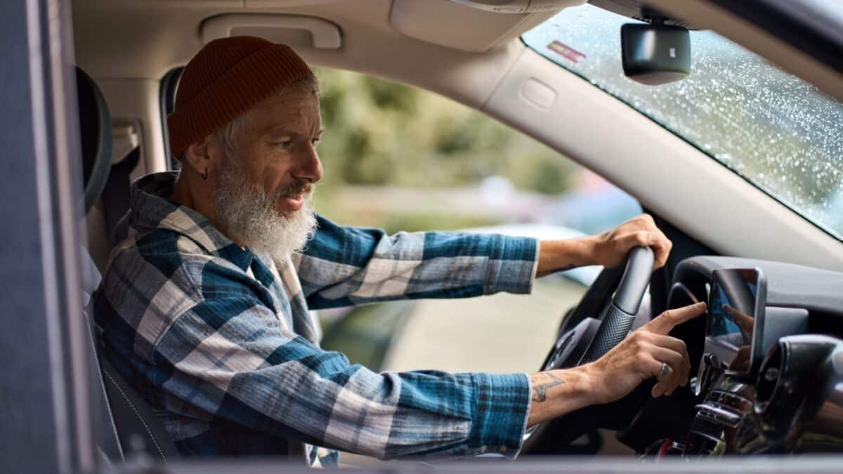 Older man sitting in camper van using gps navigation map system digital device. Smiling mature active traveler driving car vehicle looking at screen touching sensor gadget dashboard on the way.