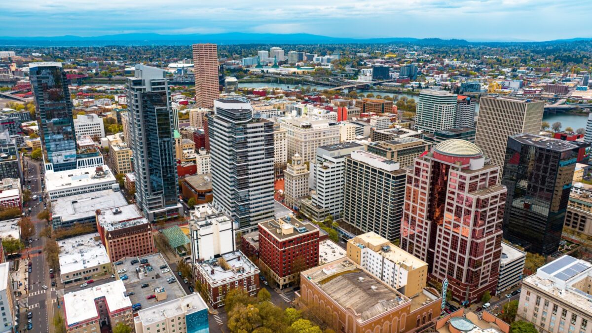 Downtown of Portland, Oregon, the USA with high-rise architecture. Twilight view of the city with mountain silhouettes at backdrop.