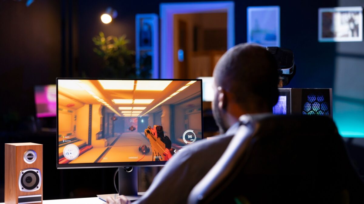 Man in living room playing video games on gaming PC at computer desk, enjoying day off from work. Gamer battling enemies in online multiplayer shooter from neon lights ornate home