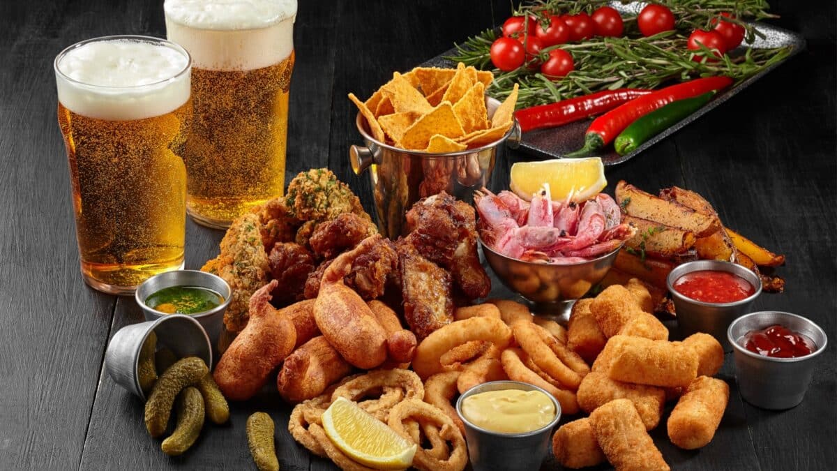 Two glasses of beer with savory snacks and vegetables on black