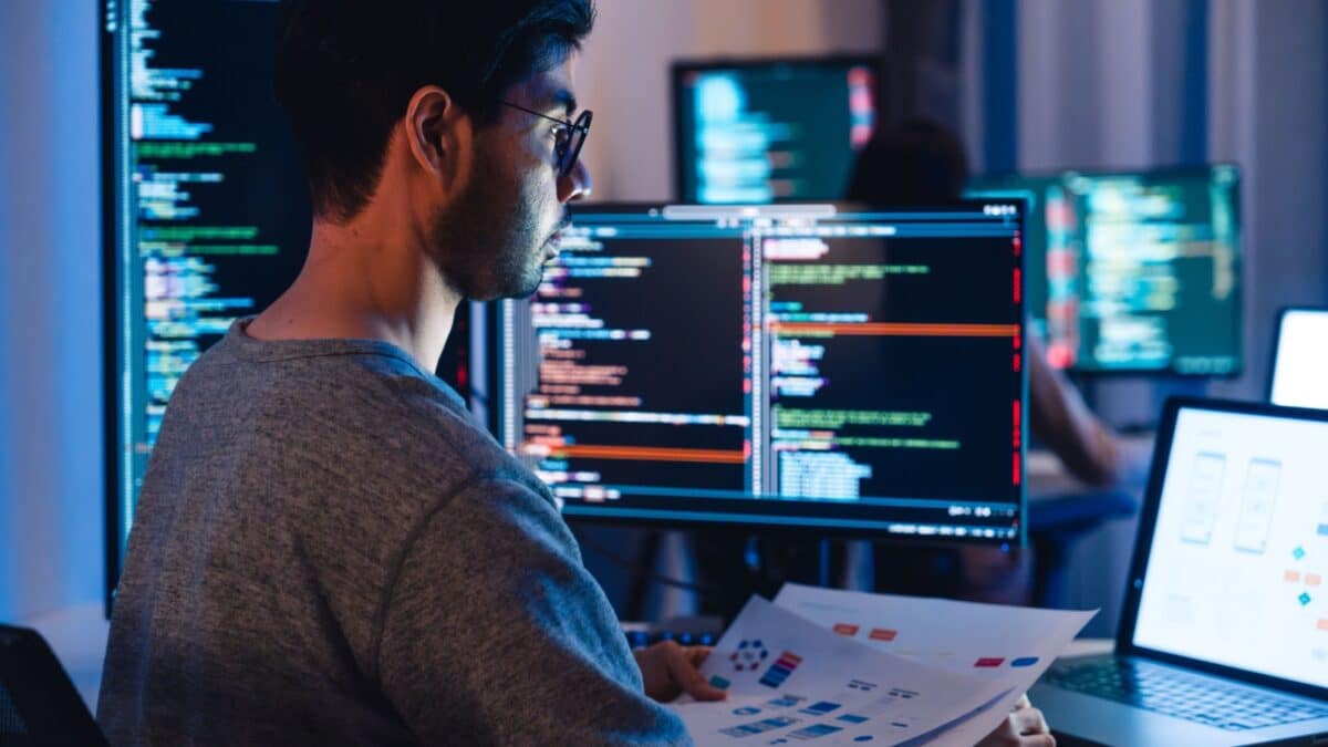 Asian software developers working on multiple screens displaying code and application diagrams at night in modern office