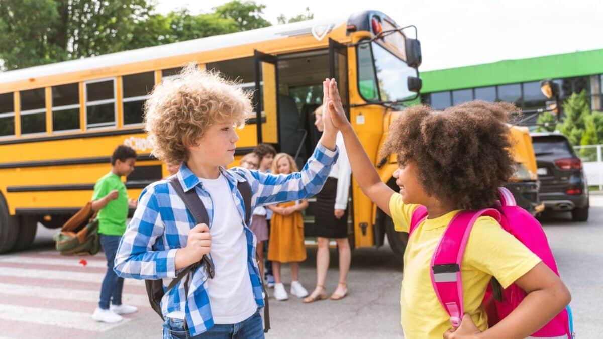 Group of young students driving to primary school on a yellow school bus - Elementary school kids having fun on a school trip