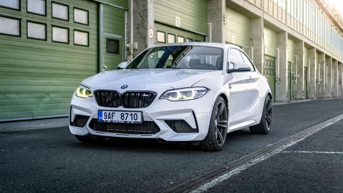 Brno, Czech Republic - October 15, 2024: White sports car BMW M2 outside on the road in front of a garage house. Fast German car in the parking lot.