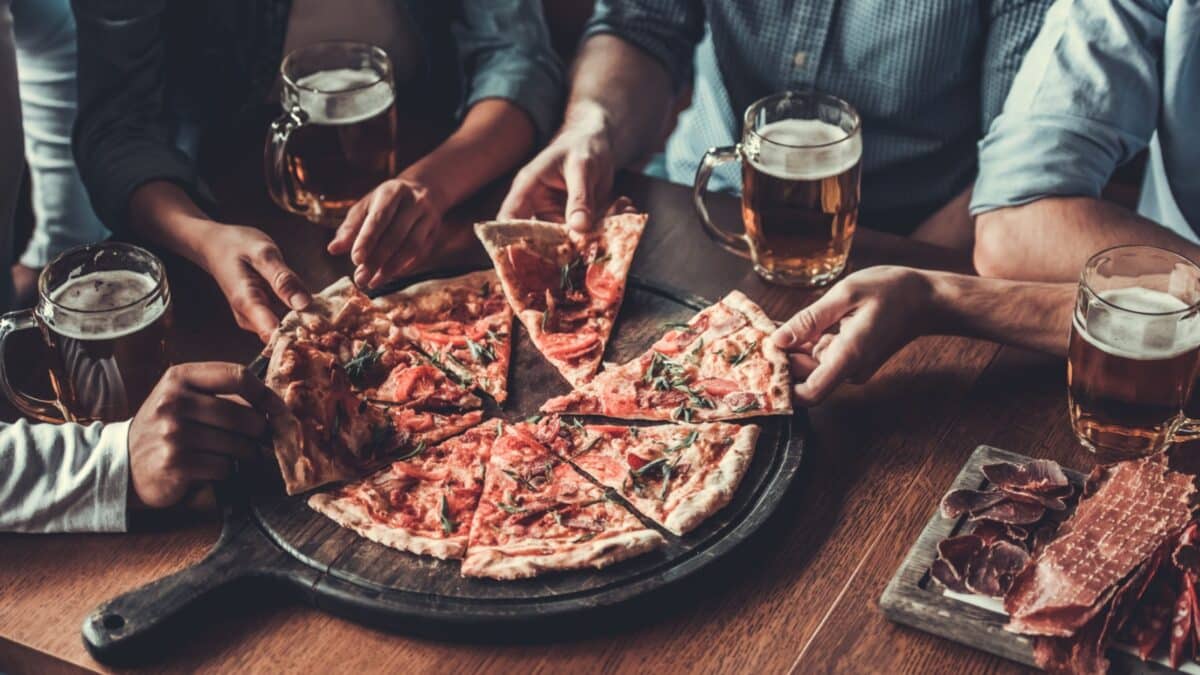 Close-up of handsome young friends drinks beer and eating pizza at pub.