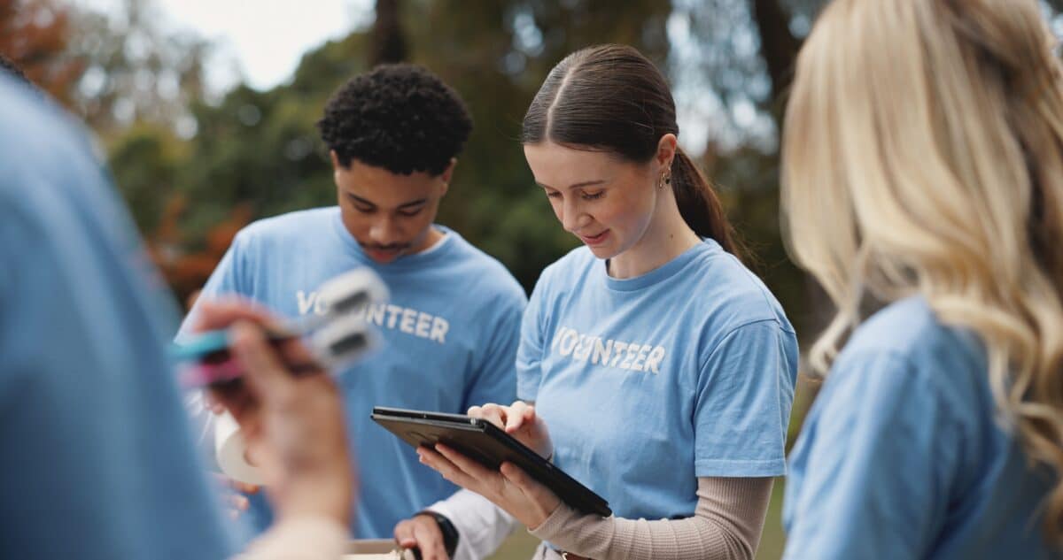 Tablet, volunteer and people in park for charity event, community service and teamwork. Volunteering, ngo group and men and women on digital tech for social media, website and online inventory