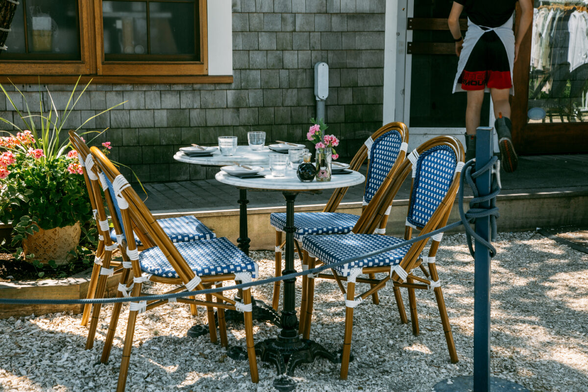 An outdoor dining table at a restaurant in nantucket, decorated with flowers and cute upholstered blue chairs